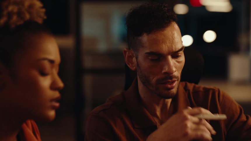 Close-up of two diverse creative professionals in a focused discussion during a late-night work session