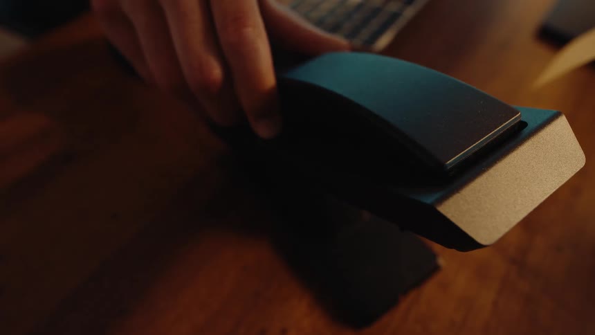 Close-up of a hand hanging up a modern black landline telephone receiver on a wooden desk