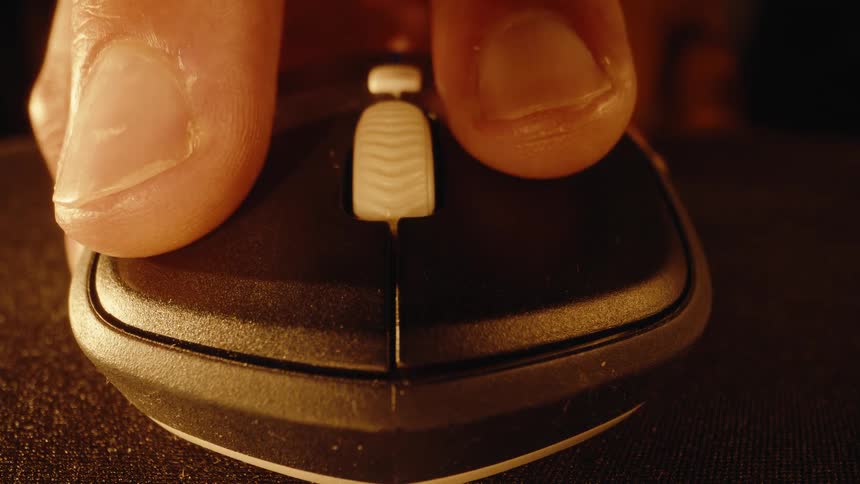 An extreme close-up shot shows a hand clicking on a computer mouse with warm, dramatic lighting