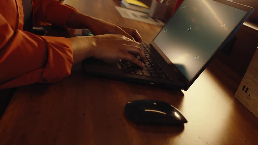 A close-up camera pull back reveals a person's hands typing on a laptop with a green screen at a wooden desk