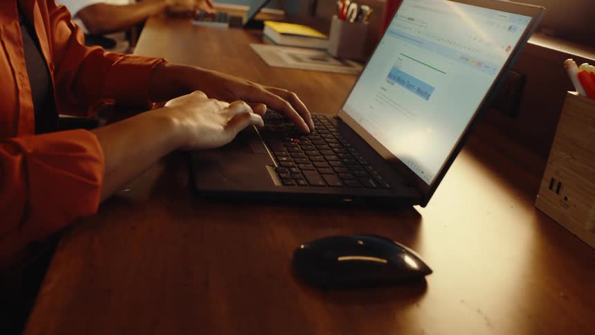 Close-up dolly shot of a person's hands typing on a laptop to prepare notes for a 'Social Media Team Meeting' at an office desk