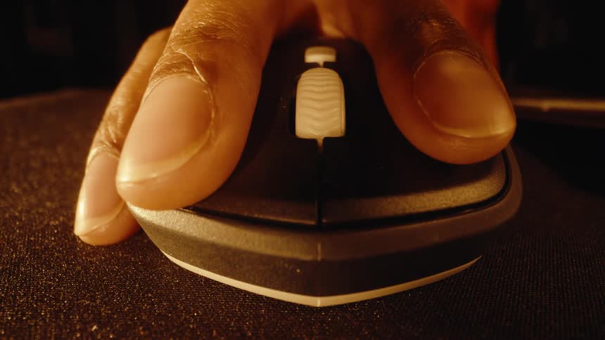 Extreme close-up of a hand moving in to operate a computer mouse on a dusty mousepad in a dimly lit room