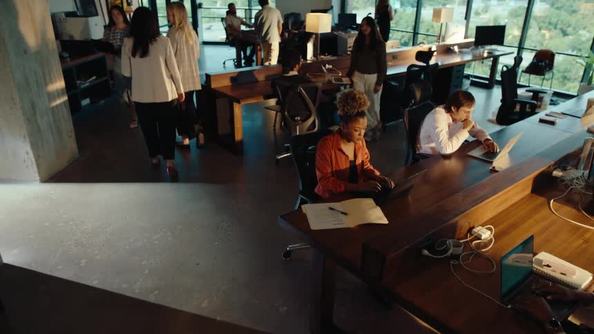 Crane shot pulls back from a focused young woman signing a document to reveal a diverse team working in a modern open-plan office