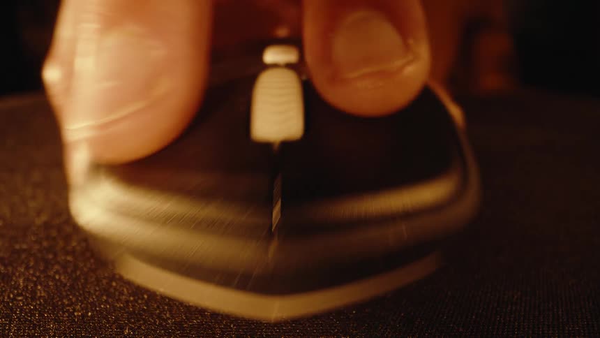 A dramatic macro shot of a hand clicking and moving a computer mouse on a dusty mousepad