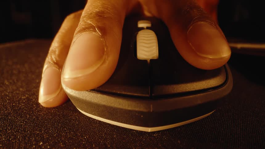 A dramatic macro shot pushes in on a hand using a wireless computer mouse on a dark mousepad