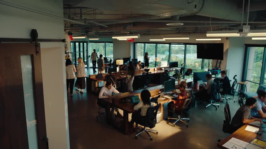 High-angle tracking shot follows an employee walking into a bustling, modern open-plan office space