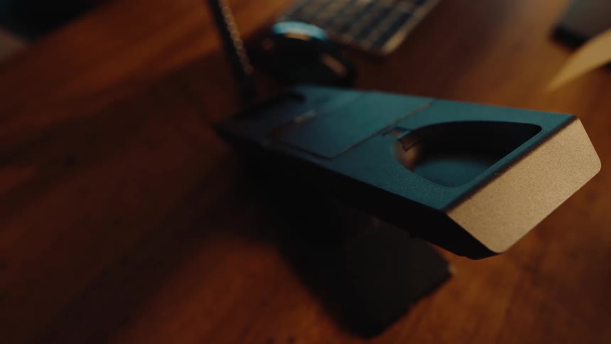 A hand picks up and hangs up a modern black landline telephone receiver on a wooden desk in a dimly lit room