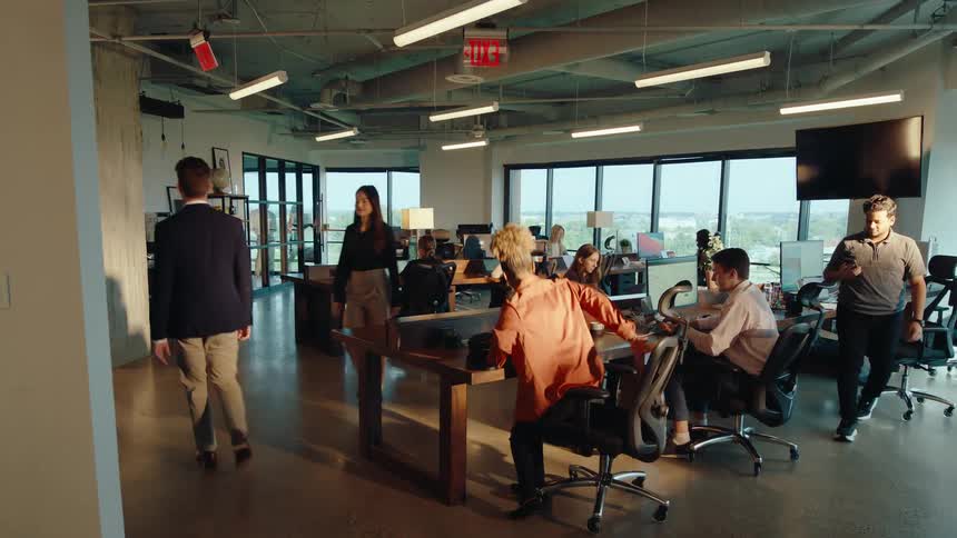 A young professional woman walks through a modern open-plan office in slow motion to her desk to begin the workday