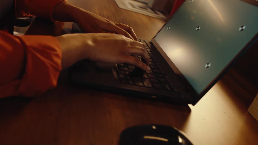 A person's hands type on a laptop with a green screen, sitting at a wooden desk in an office setting