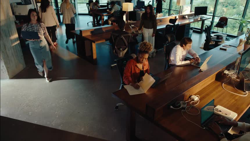 Wide high-angle shot of a diverse team working collaboratively in a modern, sunlit open-plan office