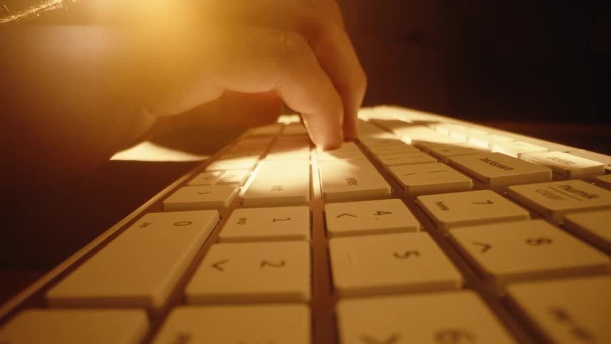 A dramatic, warm-lit, low-angle dolly shot of fingers typing on a white computer keyboard