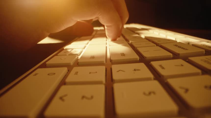 A dramatic, warm-lit macro push-in shot of a finger typing on a computer keyboard in the dark
