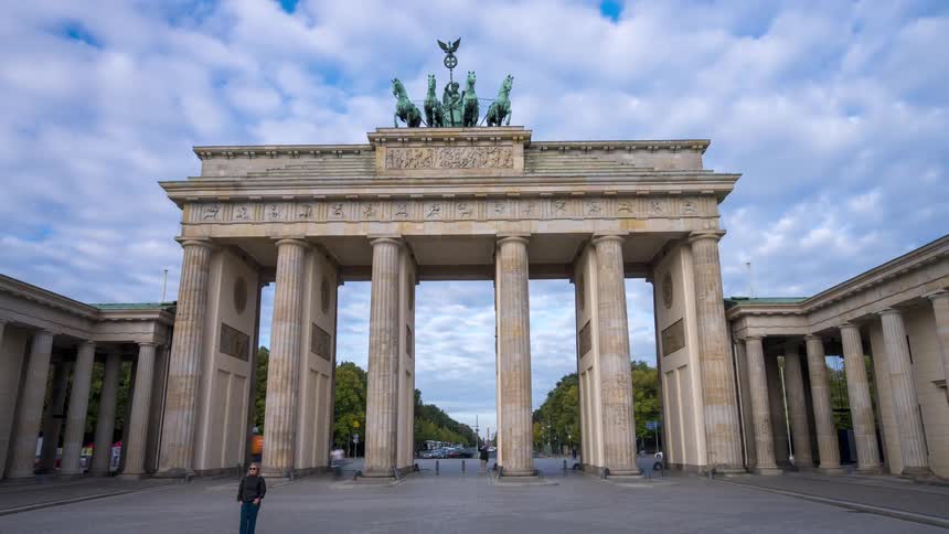 A moving time-lapse of the iconic Brandenburg Gate in Berlin as people and traffic rush by under a cloudy sky