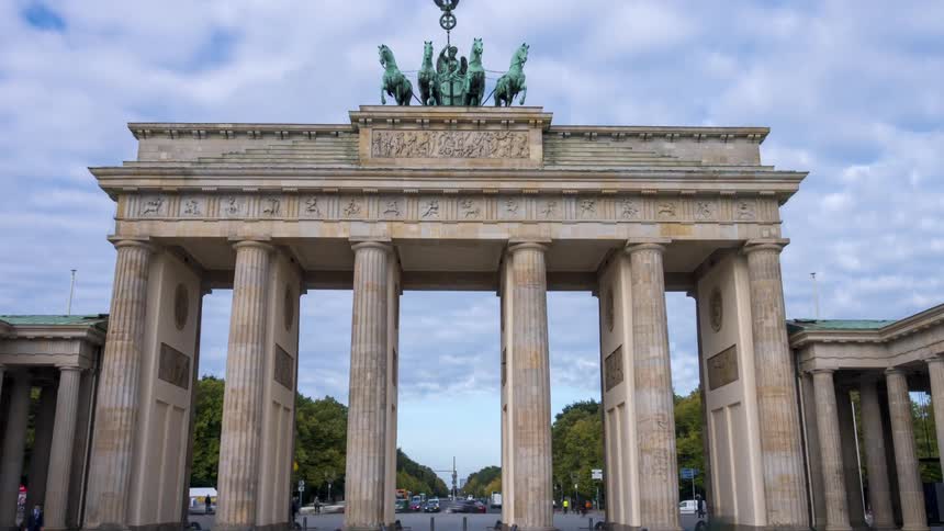 A zooming timelapse captures the historic Brandenburg Gate in Berlin as people and traffic move quickly under a cloudy sky