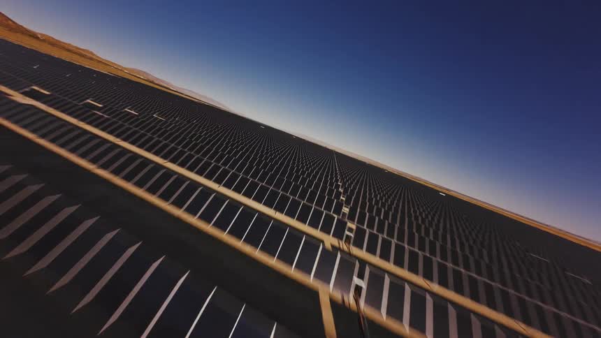 Dynamic FPV drone footage soars over a vast solar power plant under a clear blue sky