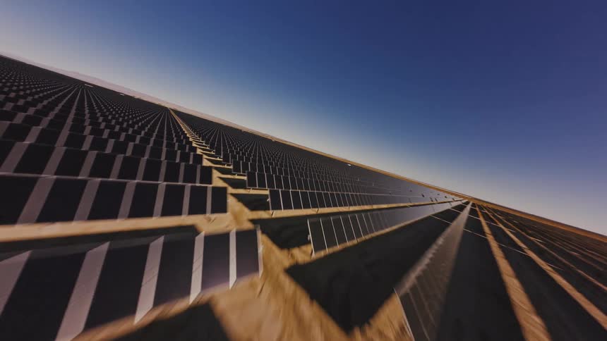 An FPV drone soars at high speed over a vast expanse of solar panels at a desert solar energy farm