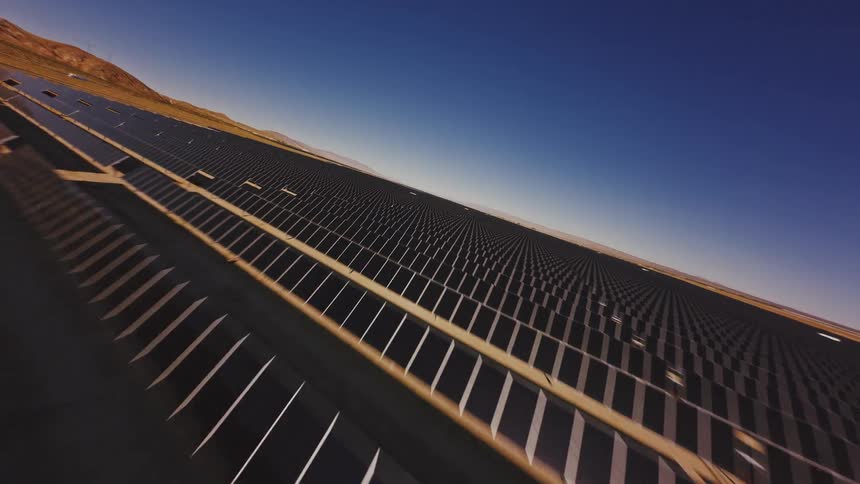A dynamic FPV drone flies low and fast over endless rows of solar panels at a massive solar farm in the desert