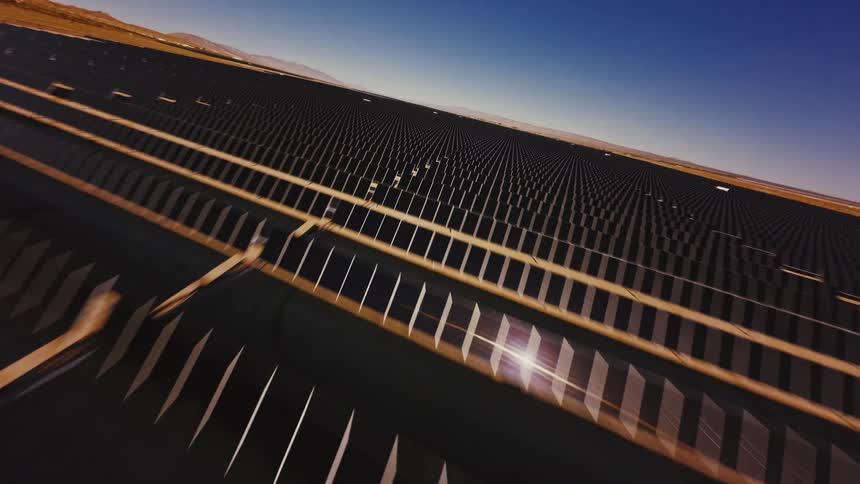 A fast-paced, canted aerial shot flies low over endless rows of solar panels at a massive solar farm in the desert