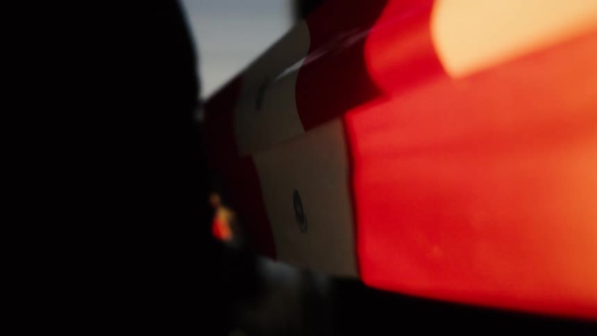 A silhouetted person holds a Canadian flag as it gently waves in the breeze against the backdrop of a beautiful, warm sunset