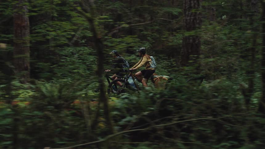 An adventurous man and woman ride their bicycles on a trail through a lush, green forest