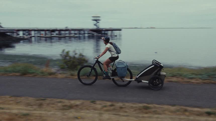 An adventurous couple on a bicycle tour ride with gear trailers along a scenic coastal path on a cloudy day