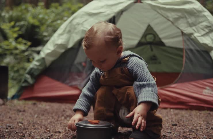 Slow motion close-up of a curious toddler carefully putting a lid on a camping pot at a forest campsite