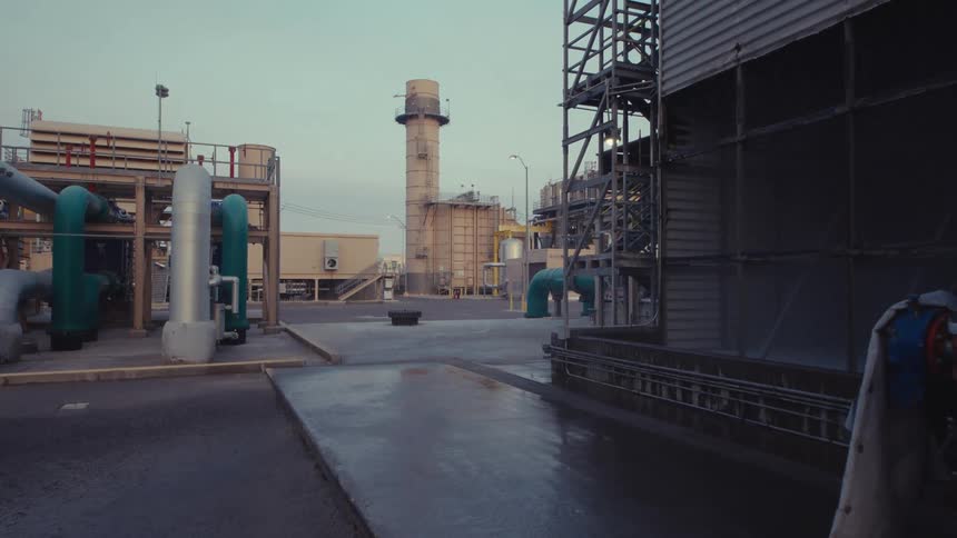 A slow, upward-tilting shot reveals the exterior of an industrial power plant at dusk