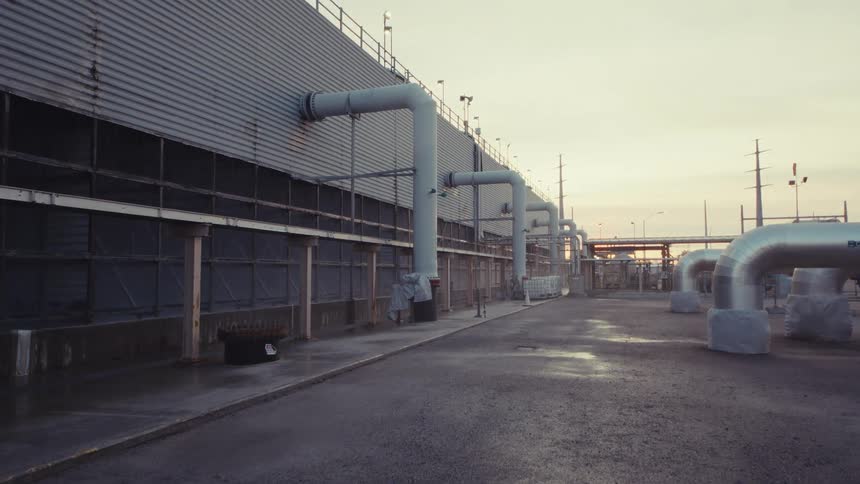 A slow tilt up from a manhole cover reveals a large industrial plant with extensive piping at dusk