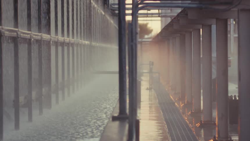 Slow tilt reveals a vast industrial water cooling system with spraying water and steam at sunset