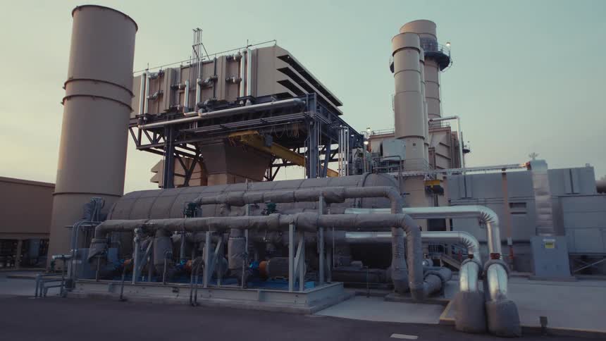 A slow, cinematic upward tilt reveals the complex network of pipes, turbines, and smokestacks at a modern power plant