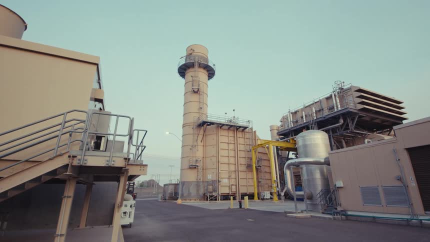 A slow dolly shot reveals the exterior grounds of a large industrial power plant with a prominent smokestack