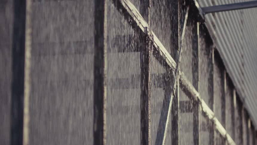 Water cascades down the textured exterior of an industrial cooling tower in a slow-motion pan shot