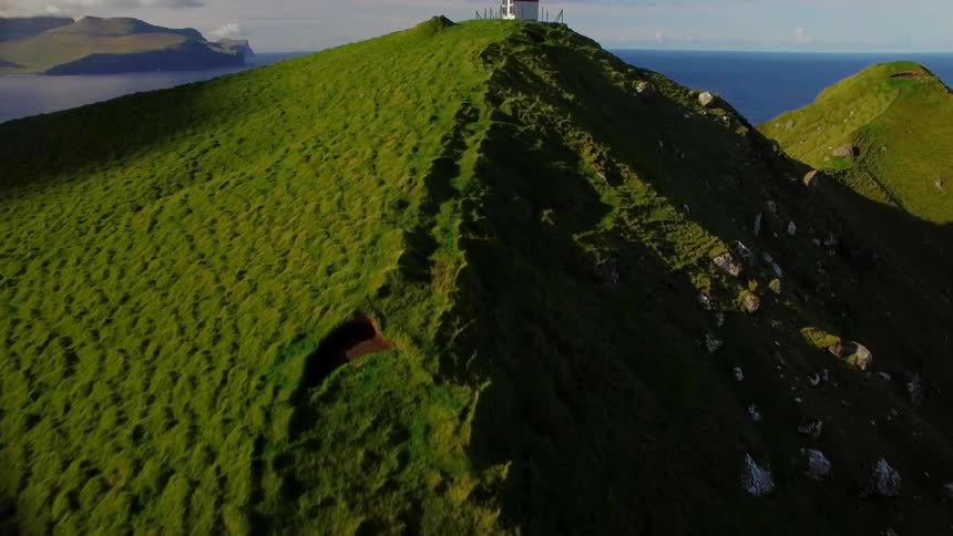 The tall green mountain has a path leading up to a building