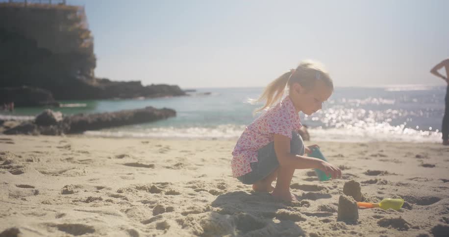 A little girl in slow motion plays with her bucket and shovel, building a sandcastle on a beautiful sunlit beach