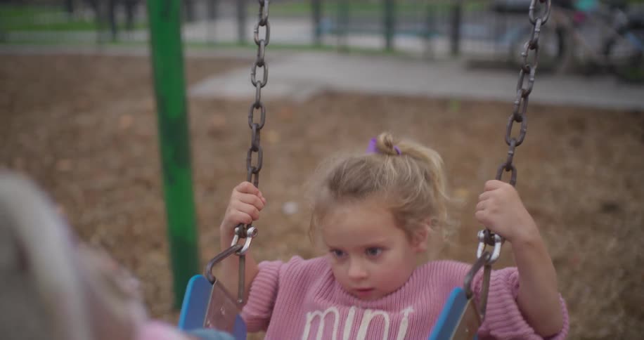 A cute toddler with blonde hair on a swing set comes into focus in this slow motion shot