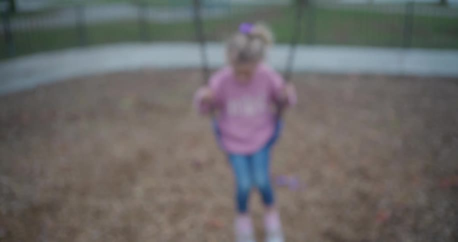 A cute little girl with blonde hair swings at a playground, coming into focus in slow motion with a sweet smile