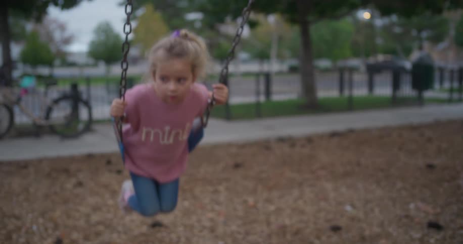 A dreamy slow-motion close-up of a cute little girl swinging at a park on an overcast day