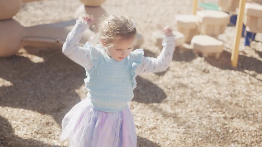 Slow motion of an adorable little girl with braided pigtails dancing and spinning at a sunny playground