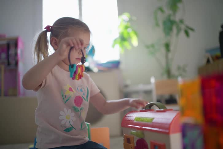 A cute little girl with pigtails plays intently with a colorful toy vet clinic, opening it up and using toy keys in slow motion