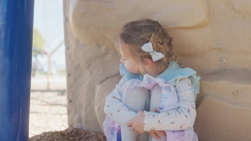 A sweet little girl looks sad while sitting alone at the playground before looking at the camera with a happy smile
