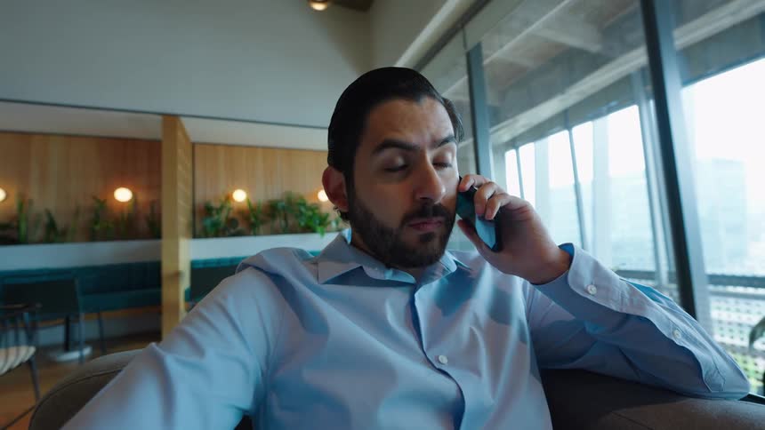 A focused businessman answers his smartphone while sitting in a contemporary office lounge