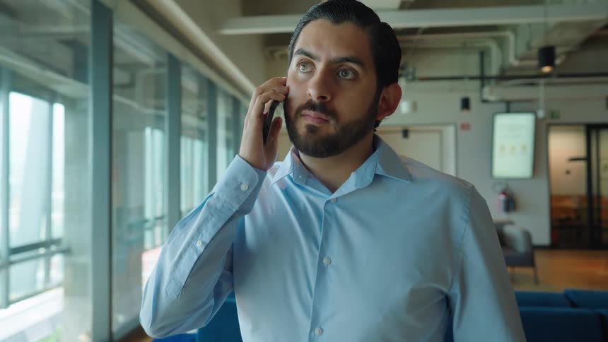 A handsome businessman in a modern office smiles while talking on his smartphone near a window