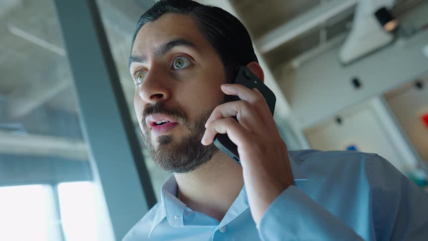 A businessman in a modern office reacts with shock and concern while receiving an urgent phone call