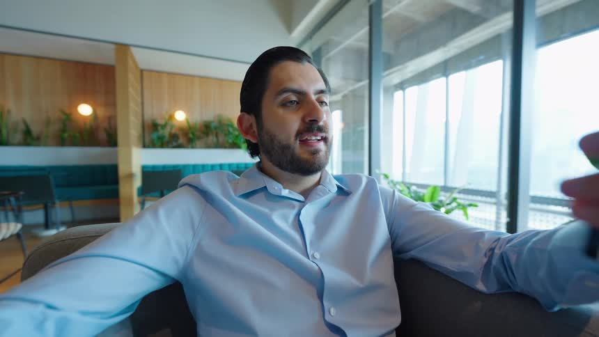 A POV slow zoom shot of a businessman smiling and talking during a video call on his smartphone in a modern office lounge