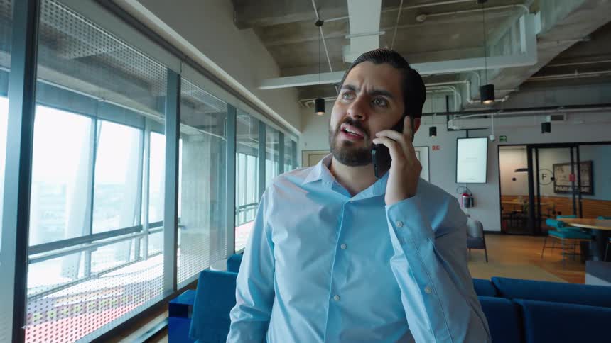 Close-up of a businessman on a phone call in a modern office, showing a range of emotions from happiness to worry