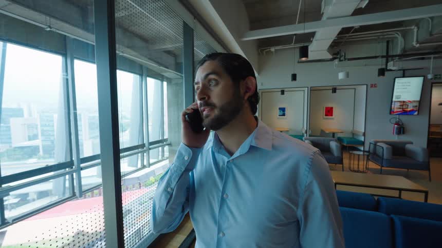 A young businessman takes a phone call while looking out the window in a modern office lounge