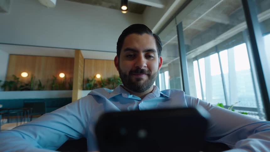 A low-angle, point-of-view shot of a smiling businessman scrolling through his smartphone in a modern office