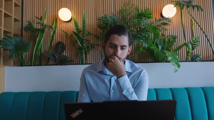 A focused businessman works on his laptop, deep in thought, in a stylish modern office with lush green plants