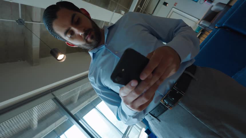 A dynamic low-angle push-in shot captures a serious businessman checking his smartphone in a contemporary office lounge