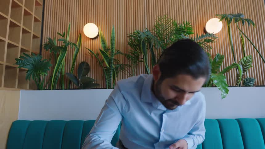 A young businessman closes his laptop and departs from a stylish, modern office space adorned with lush green plants